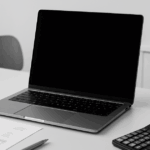 モノトーンで統一された北欧風のデスク上に、ノートパソコン、電卓、帳票、ボールペンが整然と配置されているシンプルでプロフェッショナルな会計作業風景の写真。